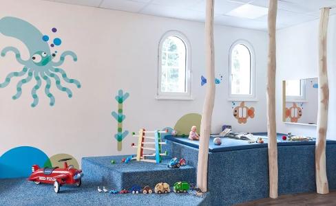 Ein heller Raum zum spielen Kita kinderzimmer Jenfelder Bach, mit Erhöhungen aus blauem Teppich bezogen und einer blauen Krake an der Wand