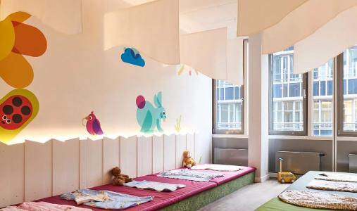 Der Schlafraum in der Kita kinderzimmer Rübenkamp mit Fenstern und bunten Tieren an der Wand sowie Matten und kleinen Decken auf dem Fußboden