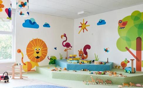 Das Spielzimmer in der Kita kinderzimmer Seebek, bunte Tiere sind an die Wand gemalt, auf Teppich liegt Spielzeug und große Fenster sorgen für Tageslicht