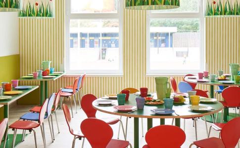 Der Raum zum Essen in der Kita kinderzimmer Seebek, bunte Stühle stehen an bunten Tischen, zwei große Fenster und bunte Lampen hängen von der Decke
