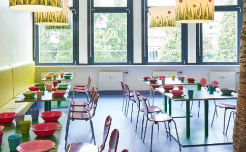 Der Raum zum Essen in der Kita kinderzimmer Stubbenhuk, bunte Stühle stehen an bunten Tischen, eine Fensterfront bietet viel Tageslicht