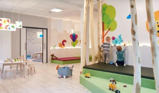 Ein Spielzimmer der Kita kinderzimmer Alsterberg mit hellem Fußboden, hellen Wänden und bunten Bäumen, Blumen und Tieren die an die Wand gemalt sind