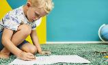 Ein Kind sitzt auf einem grünen Teppich und malt ein Bild