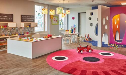 Ein großer Raum der Kita kinderzimmer Heidbrook zum spielen, mit einem Kaufmannsladen und einem großen runden Teppich mit Augen und Nase