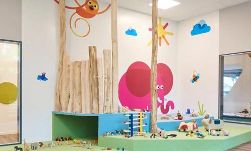 Ein Spielzimmer der Kita kinderzimmer Inselpark mit einem rosafarbenen Elefanten an der Wand und Spielzeug auf einer kleinen, mit Teppich überzogenen Anhöhe