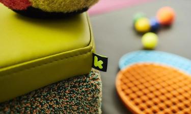 Ein grünes Sitzkissen liegt auf einem runden Teppich und daneben liegen kleine Bälle