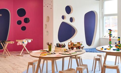 Ein Raum in der Kita kinderzimmer Seebek mit pinken, blauen und weißen Wänden, hellem Holzfußboden und kleinen Tischgruppen