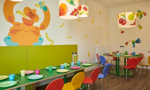 Der Raum zum Essen in der Kita kinderzimmer Vogelkamp mit einem orangefarbenen Affen und gelben Bananen an der Wand, bunte Stühle und Tische stehen davor