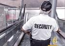 Ein Mann mit weißem Tshirt und schwarzer Aufschrift SECURITY steht auf einer Rolltreppe