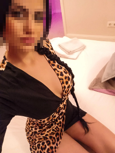 Valeria in einem schwarzen Kleid mit Leopardenmusterelementen sitzt auf einem Bett, das Gesicht wurde unkenntlich gemacht