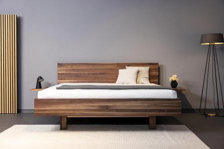 Ein Bett aus Holz vor einer grauen Wand