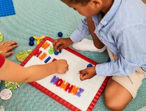 Zwei Kinder sitzen auf einem grünen Teppich und spielen mit Buchstaben