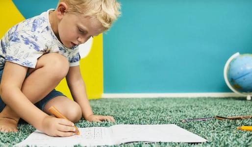 Ein Kind sitzt auf einem grünen Teppich und malt ein Bild