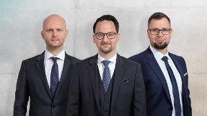 Norman Buse, David Herz und Benjamin Grunst stehen nebeneinander in Anzügen, einem weißen Hemd und einer blauen Krawatte