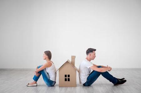 Ein Mann und eine Frau sitzen mit dem Rücken an einem kleinen Haus