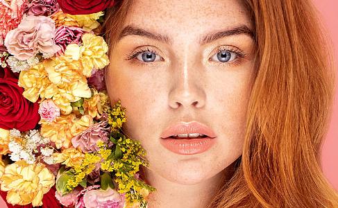 Eine Frau mit blauen Augen, roten Haaren und Sommersprossen neben einem bunten Strauß Blumen