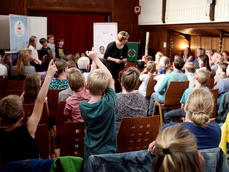  Autorin Ursula Flacke in Interaktion mit den Schulkindern in einem Saal.