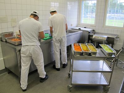  Zwei Männer in weißer Kleidung stehen vor einer Gastronomie Küchentheke und schneiden Gemüse