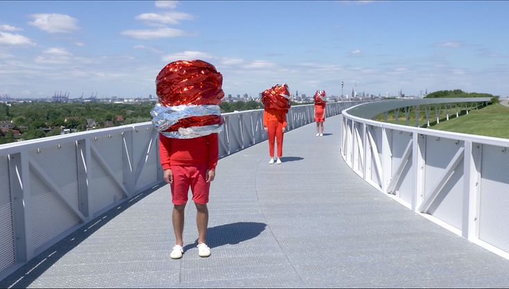 drei Menschen in roter Sportkleidung und großflächig mit Plastik verhüllten Köpfen