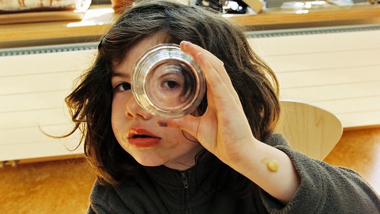 Kita: Ein Kind schaut neugierig durch ein Glas