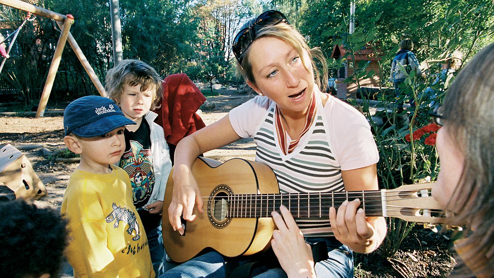 Eine Frau spielt Kindern auf der Gitarre vor