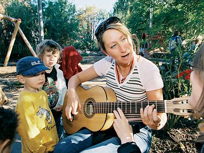  Eine Frau spielt Kindern auf der Gitarre vor