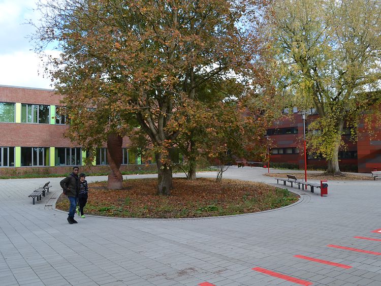  Zwei Schüler auf dem Schulhof vor einer Gruppe Bäume