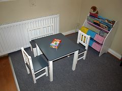  Ein Tisch mit drei Stühlen stehen in einer Ecke vor einem Heizkörper und einem Regal mit Büchern.