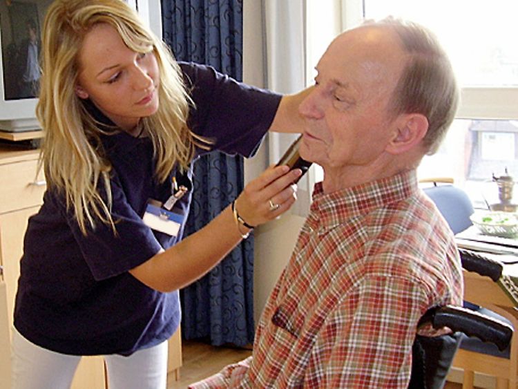  Eine Pflegerin rasiert einen Mann im Rollstuhl