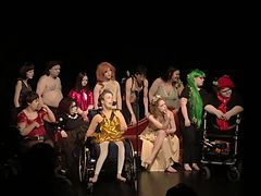 Eine Gruppe phantasievoll gekleideter junger Schauspieler auf der Bühne, einige in Rollstühlen