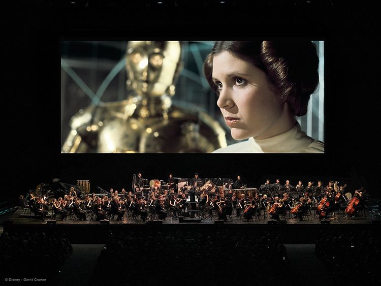  Auf der Bühne spielt ein Orchester, im Hintergrund läuft ein Star Wars Film.