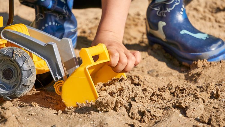  Spielzeugbagger im Sand mit Kinderhand und Kinderfüßen