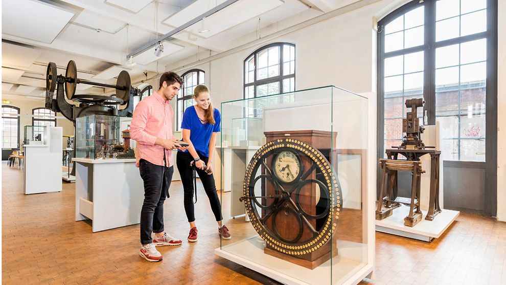 ein junges Paar betrachtet die Arbeiterkontrolluhr im Museum der Arbeit