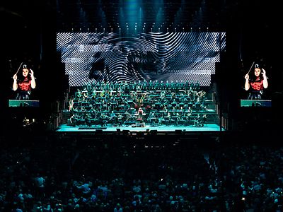 Aufnahme des Antwerp Philharmonic Orchestra auf einer großen Bühne. Das Geschehen wird auf zwei großen Leinwänden übertragen.