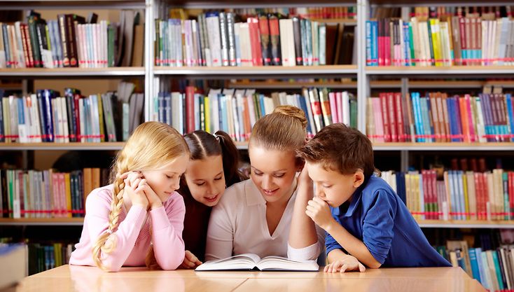Drei Kinder sitzen mit Vorleserin vor einem Bücherregal