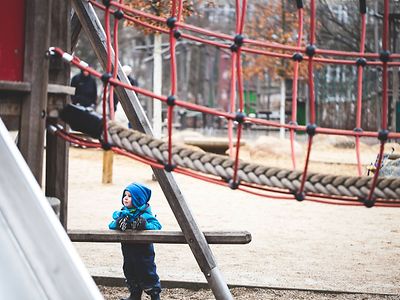  Ein Kind steht in Winterkleidung auf einem Spielplatz.