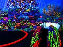  Minigolf in einer Unterwasserwelt mit Fischen und Korallenriffen, Pizza im Bistro und Menschen, die sich durch Laserstrahlen bewegen.