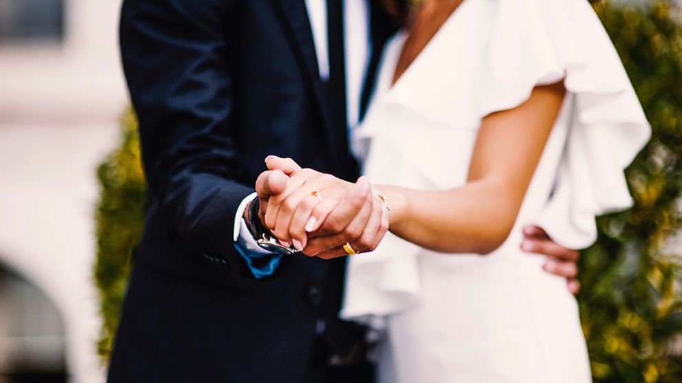  Ein Mann und eine Frau halten ihre Hände in die Kamera. Beide tragen einen goldenen Ehering.