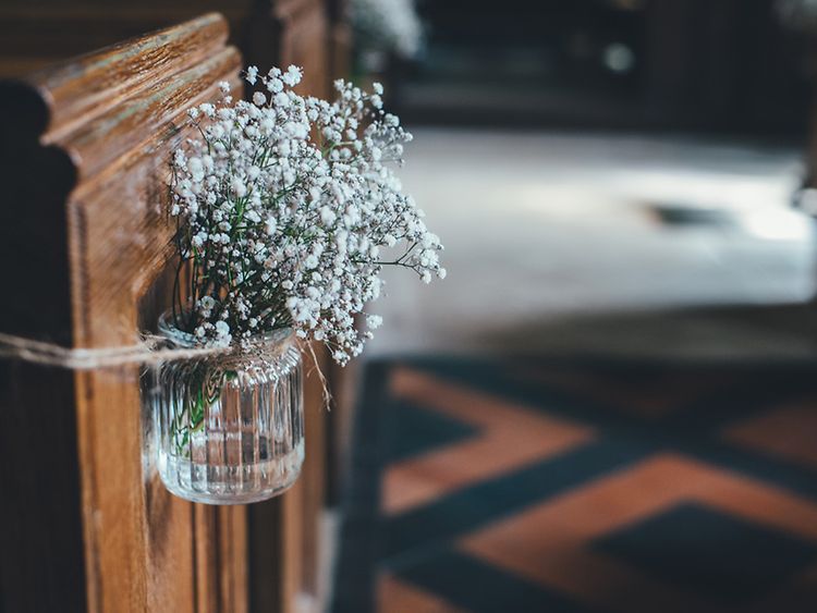  Ein Strauß mit kleinen weißen Blumen ist an einer Kirchenbank angebunden.