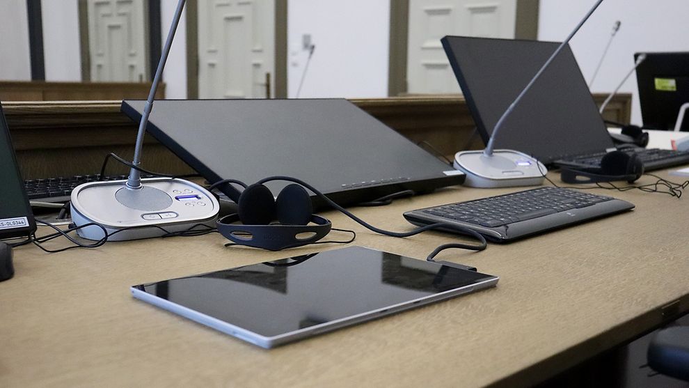  Mehrere elektronische Geräte stehen auf einem Tisch: Bildschirme, ein Tablet, Mikrofone, Kopfhörer
