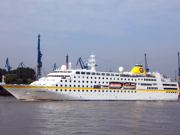  Die MS Hamburg. Weißes Kreuzfahrtschiff mit gelber Bordüre an der Bordwand.