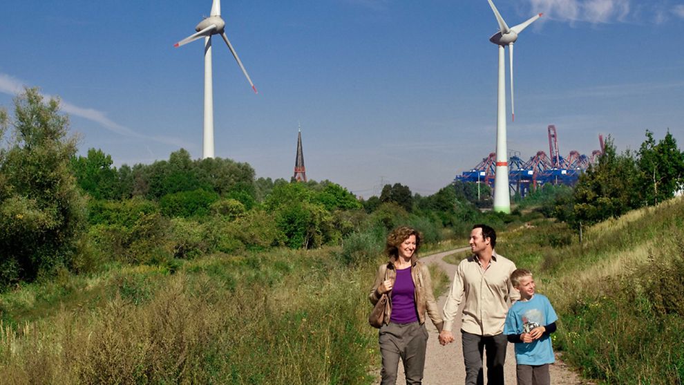  Familie spaziert auf einem Feldweg mit Windrädern im Hintergrund.