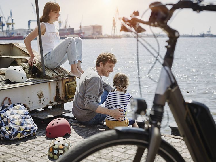  Eine Familie sitzt am Wasser, im Vordergrund ist ein Fahrrad zu sehen.