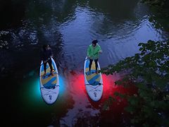  Zwei Stand Up Paddler auf dem Wasser. Unter den Boards wird das Wasser blau und rot beleuchtet.