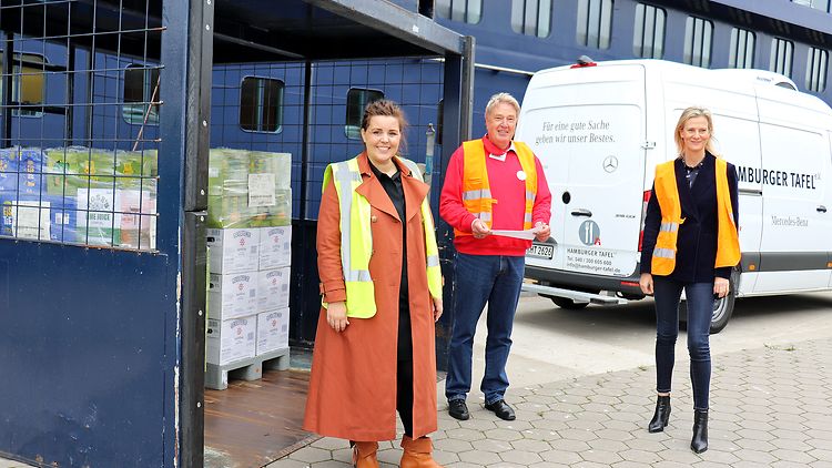  Drei Personen stehen vor einem Container mit Lebensmitteln und einem Transporter.