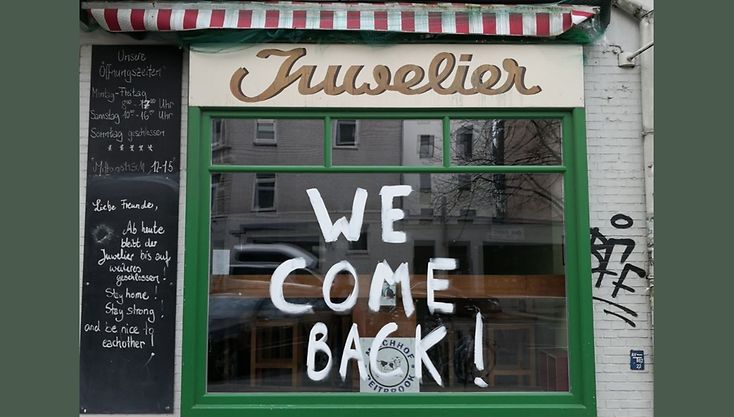 Ein Ladenfester auf das in Großbuchstaben geschrieben steht: We Come Back! 