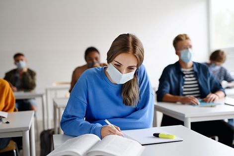 Eine Schülerin in der Schulklasse mit einem Mund-Nasen-Schutz arbeitet am Tisch