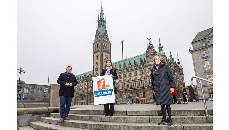 Senator Dr. Carsten Brosda, Dorit Otto und Gesa Engelschall mit einem Plakat auf den Stufen vor dem Hamburger Rathaus