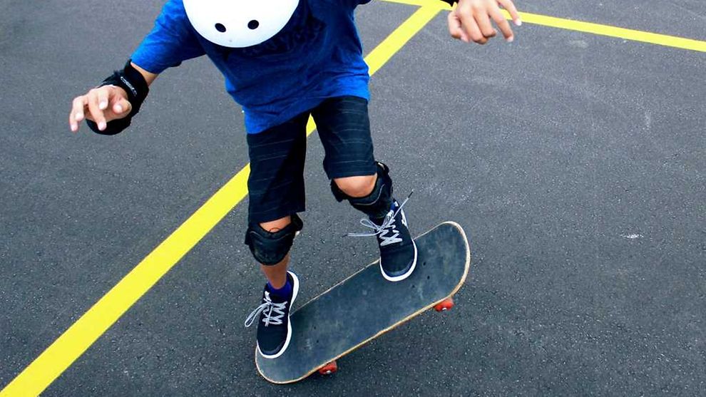  Ein Kind mit Helm und Knie- und Ellenbogenschonern fährt auf einem Skateboard.