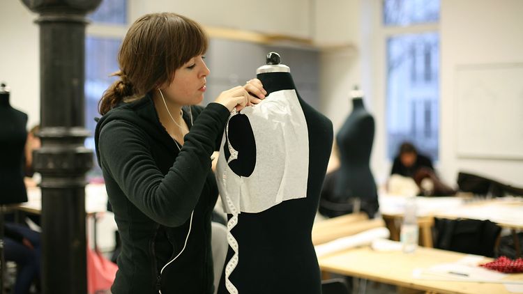  Junge Frau arbeitet stehend an einer Kleiderpuppe in einem Atelier für Modedesign